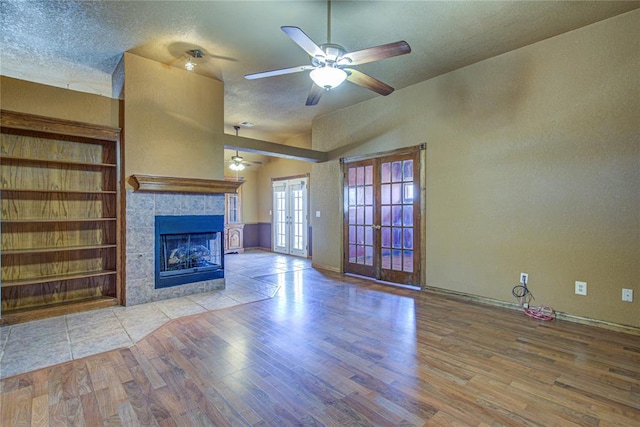 unfurnished living room with french doors, a textured ceiling, a tiled fireplace, and wood finished floors