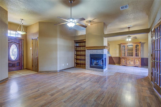 unfurnished living room featuring a textured ceiling, wood-type flooring, a fireplace, and visible vents