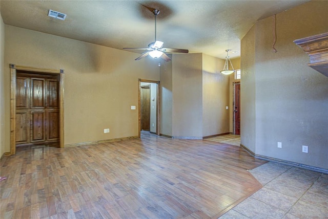 spare room with baseboards, visible vents, a ceiling fan, wood finished floors, and a textured ceiling