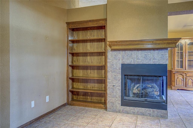 unfurnished living room with built in shelves, a tile fireplace, and baseboards