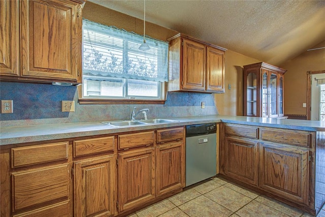 kitchen with brown cabinetry, light countertops, stainless steel dishwasher, a sink, and light tile patterned flooring