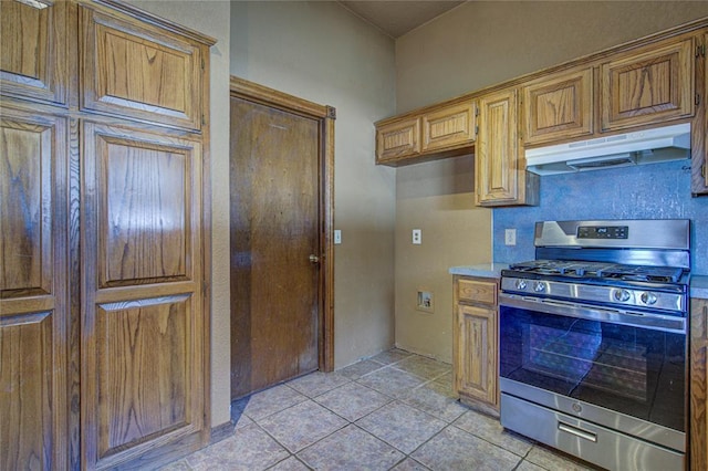 kitchen featuring light tile patterned floors, light countertops, brown cabinetry, gas range, and under cabinet range hood