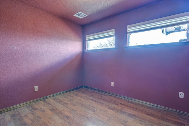 empty room featuring a textured ceiling, wood finished floors, and visible vents