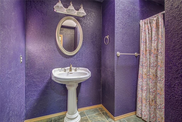 full bath featuring curtained shower, baseboards, and a textured wall