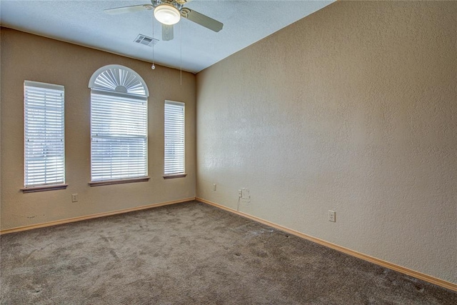 unfurnished room with a textured wall, carpet floors, visible vents, baseboards, and a ceiling fan