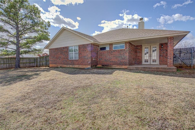 exterior space featuring french doors, brick siding, a yard, a chimney, and fence