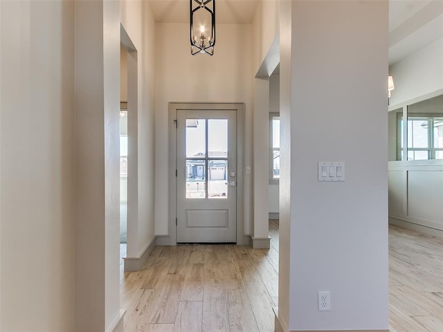 entryway featuring baseboards, light wood-type flooring, and an inviting chandelier