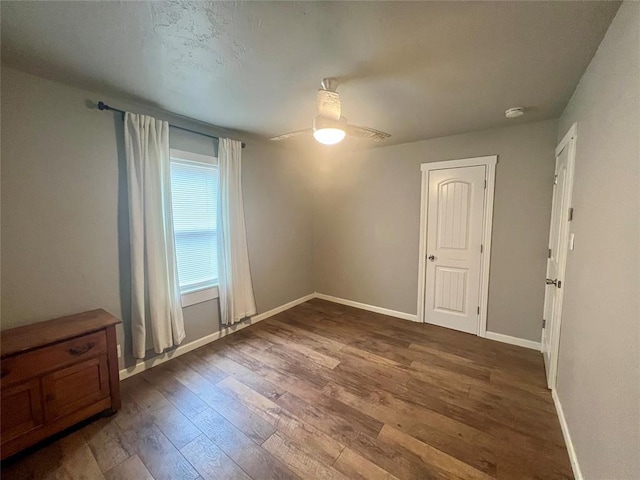 empty room featuring ceiling fan, baseboards, and dark wood-style flooring