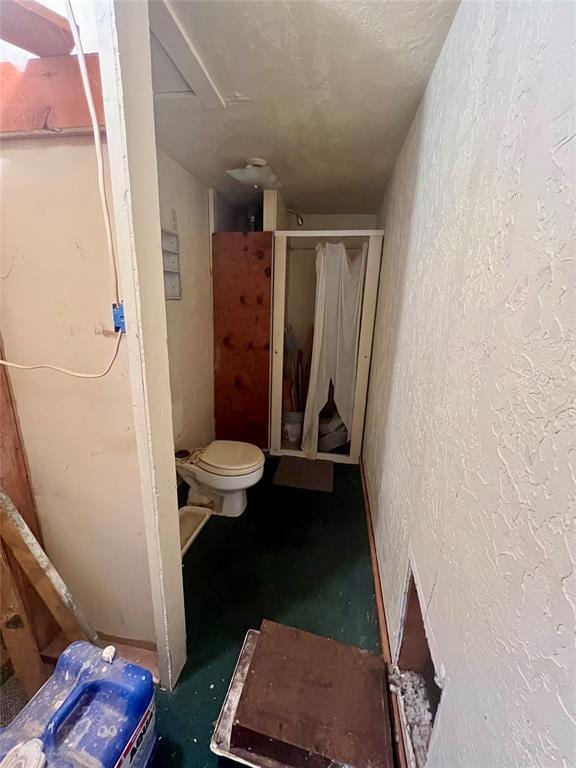 full bathroom featuring a stall shower, a textured wall, a textured ceiling, and toilet