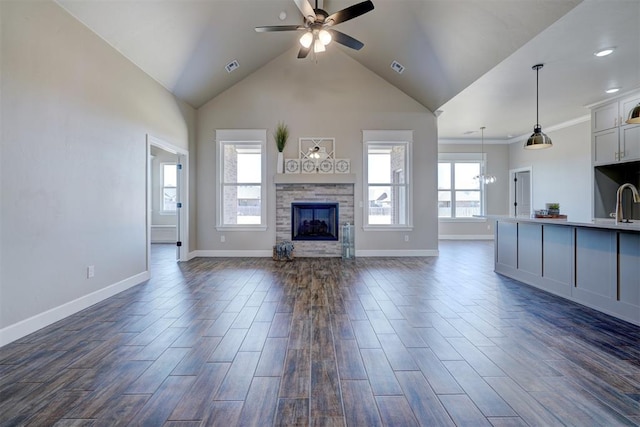 unfurnished living room with a wealth of natural light, a stone fireplace, dark wood finished floors, and a ceiling fan