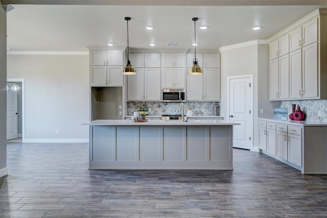 kitchen featuring light countertops, stainless steel microwave, crown molding, and an island with sink