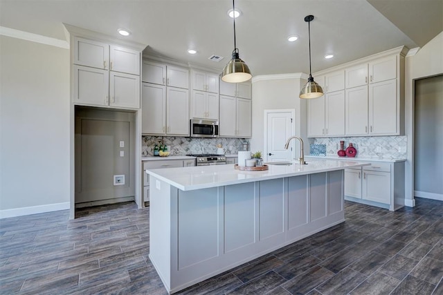 kitchen featuring a sink, visible vents, appliances with stainless steel finishes, wood tiled floor, and a center island with sink