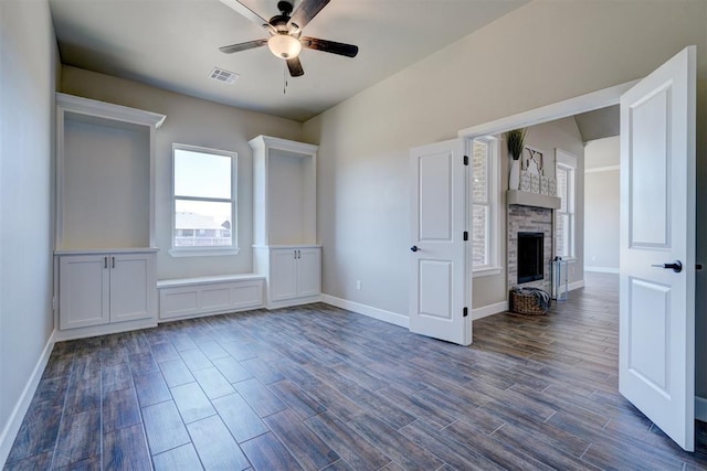 unfurnished bedroom with dark wood finished floors, a fireplace, baseboards, and ceiling fan