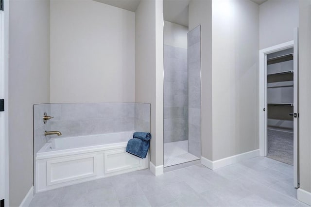 bathroom with a tile shower, baseboards, and a bath