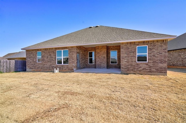 back of house featuring brick siding, fence, a yard, roof with shingles, and a patio area