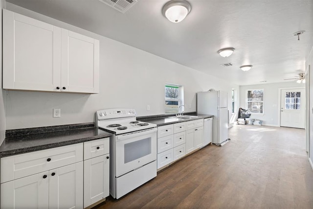 kitchen with dark countertops, white appliances, visible vents, and a sink