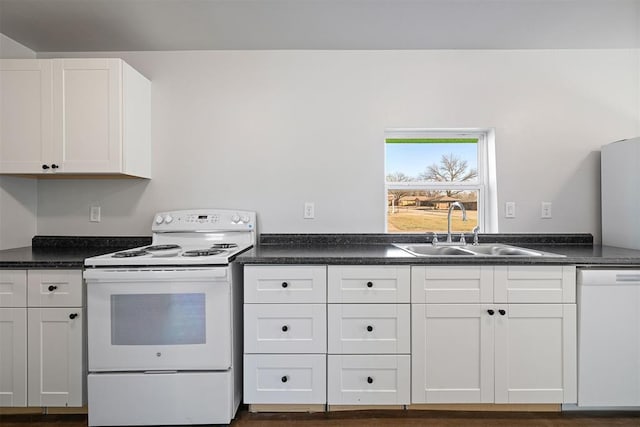 kitchen with white appliances, dark countertops, a sink, and white cabinets