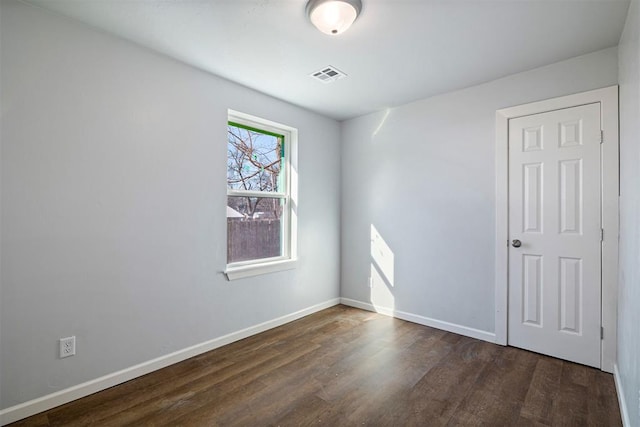 empty room with wood finished floors, visible vents, and baseboards