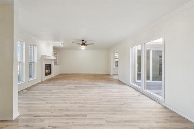 unfurnished living room with a ceiling fan, light wood-style floors, a warm lit fireplace, and ornamental molding