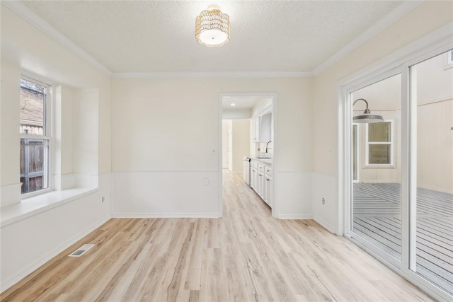 spare room with light wood finished floors, visible vents, crown molding, a textured ceiling, and a sink