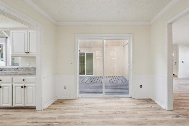 unfurnished dining area featuring crown molding, a wainscoted wall, and light wood-type flooring