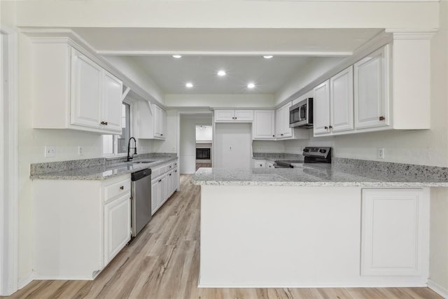 kitchen featuring a sink, white cabinetry, appliances with stainless steel finishes, a peninsula, and light stone countertops