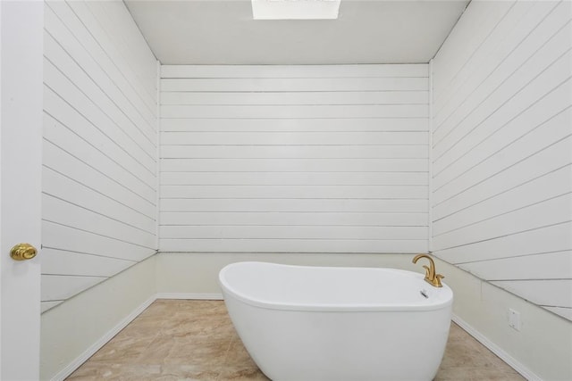 bathroom featuring wooden walls, baseboards, and a freestanding bath