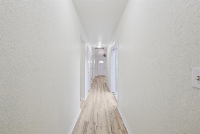 hallway with light wood-style flooring, a textured wall, and baseboards