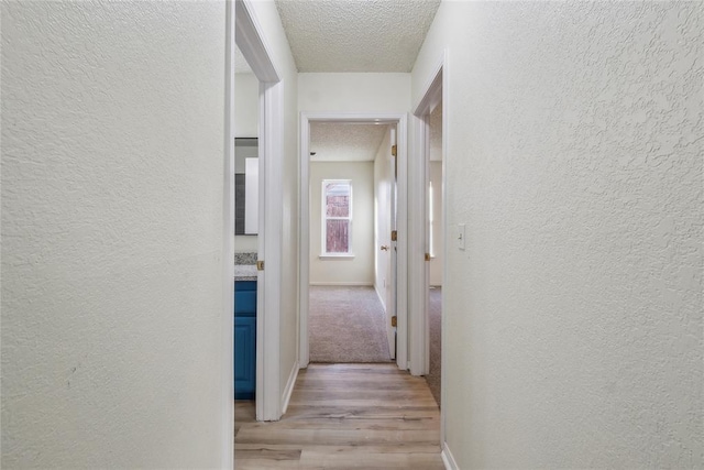 hall featuring light wood-style flooring, a textured wall, and a textured ceiling