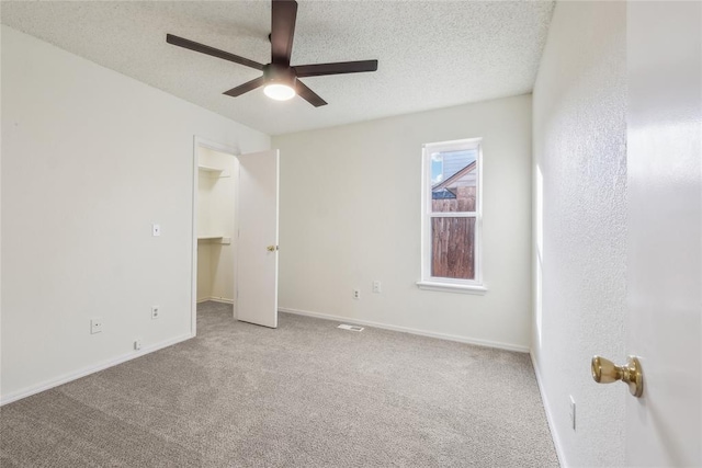 unfurnished bedroom with a walk in closet, a textured ceiling, carpet, baseboards, and ceiling fan