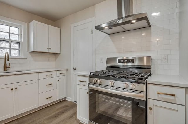 kitchen featuring stainless steel gas range oven, white cabinets, light wood-style floors, wall chimney range hood, and a sink