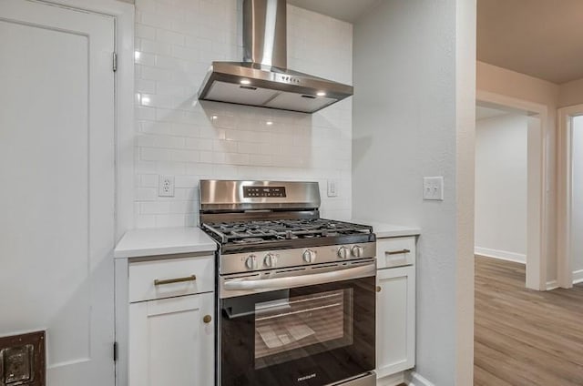 kitchen featuring white cabinets, light countertops, decorative backsplash, stainless steel gas stove, and wall chimney exhaust hood