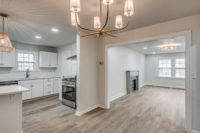 kitchen featuring under cabinet range hood, a fireplace, a sink, light countertops, and stainless steel gas range