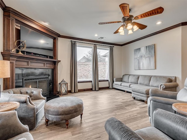 living area featuring visible vents, a ceiling fan, a tile fireplace, ornamental molding, and light wood-type flooring