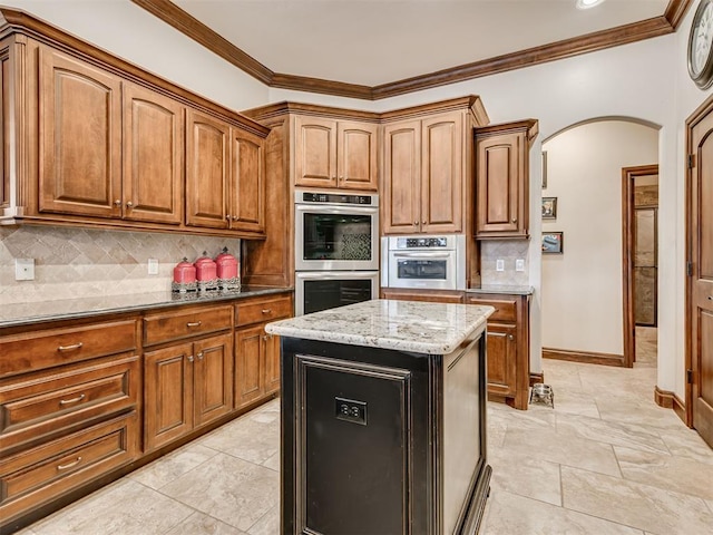 kitchen featuring arched walkways, tasteful backsplash, stainless steel double oven, and brown cabinets