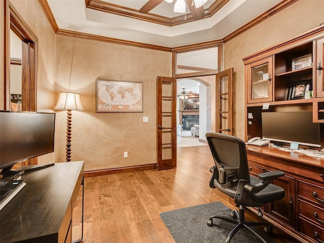 office area with arched walkways, crown molding, a fireplace, light wood-style floors, and ceiling fan