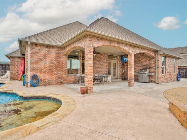 back of property featuring brick siding, roof with shingles, a patio area, and an outdoor pool