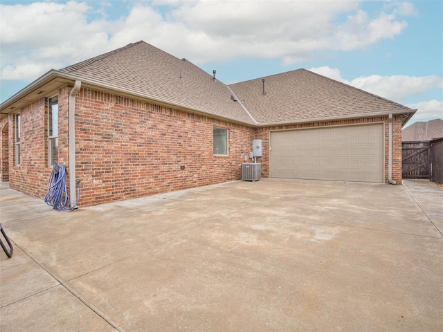 view of side of property with central air condition unit, driveway, a shingled roof, and brick siding