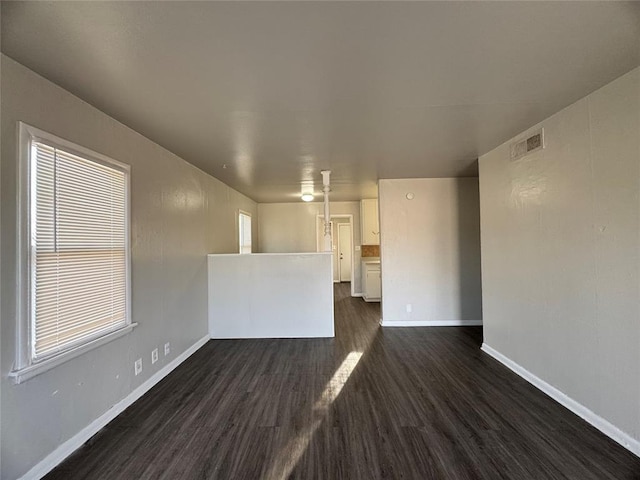 unfurnished room with a wealth of natural light, baseboards, visible vents, and dark wood-type flooring