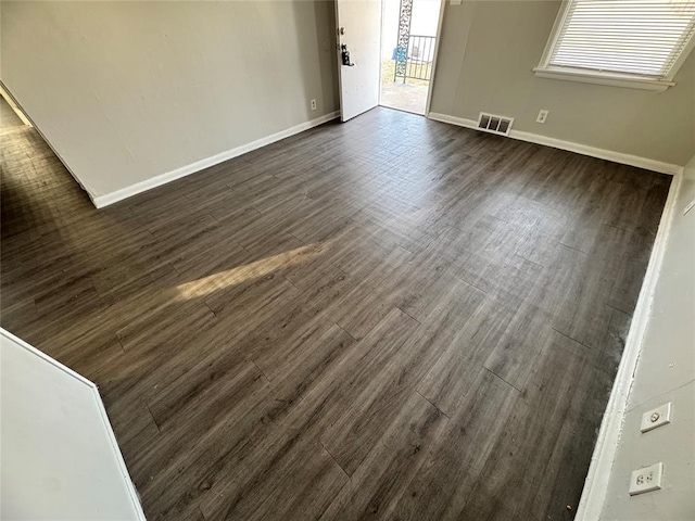 unfurnished room featuring dark wood-style flooring, visible vents, and baseboards