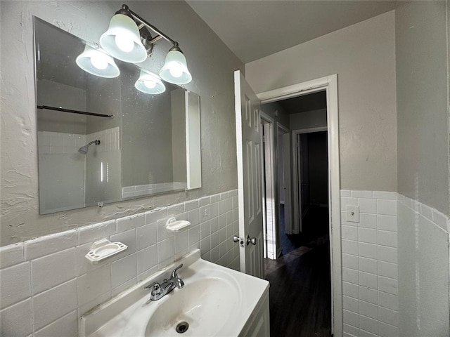 bathroom with a shower, a wainscoted wall, tile walls, and vanity