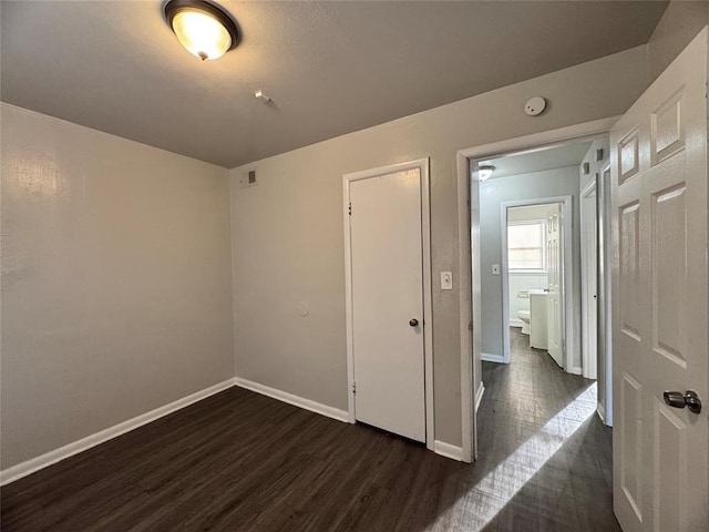 unfurnished bedroom featuring visible vents, dark wood finished floors, and baseboards