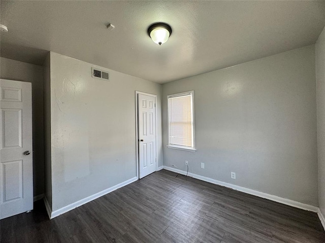 spare room with dark wood-style floors, visible vents, and baseboards