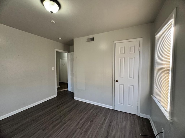 unfurnished bedroom featuring dark wood-style floors, visible vents, and baseboards