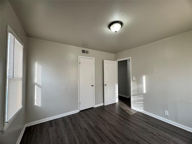 unfurnished bedroom with visible vents, dark wood finished floors, and baseboards