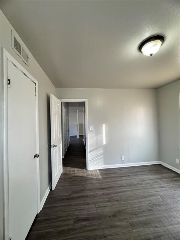 unfurnished room featuring dark wood-type flooring, visible vents, and baseboards