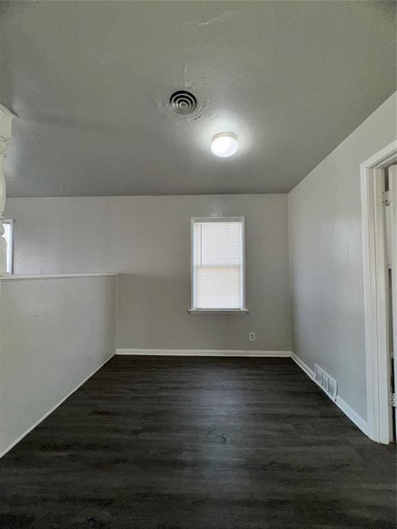 spare room with dark wood-style flooring, visible vents, and baseboards