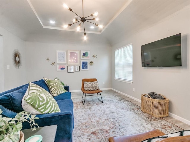 living area with a chandelier, a tray ceiling, wood finished floors, and baseboards