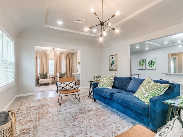 living area with light wood-type flooring, a raised ceiling, visible vents, and a notable chandelier