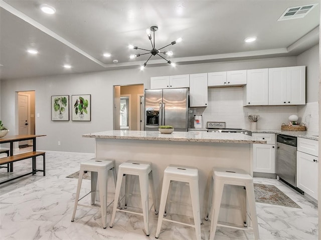 kitchen with marble finish floor, stainless steel appliances, visible vents, backsplash, and a kitchen bar